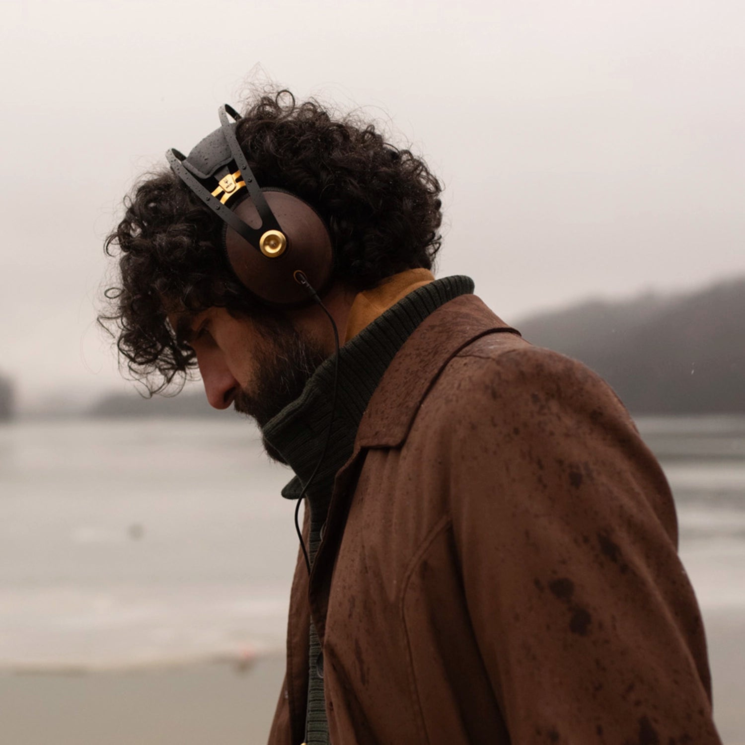 Man listening to music on his Meze Audio 99 Classics Walnut Gold premium audiophile closed back headphones near the seaside