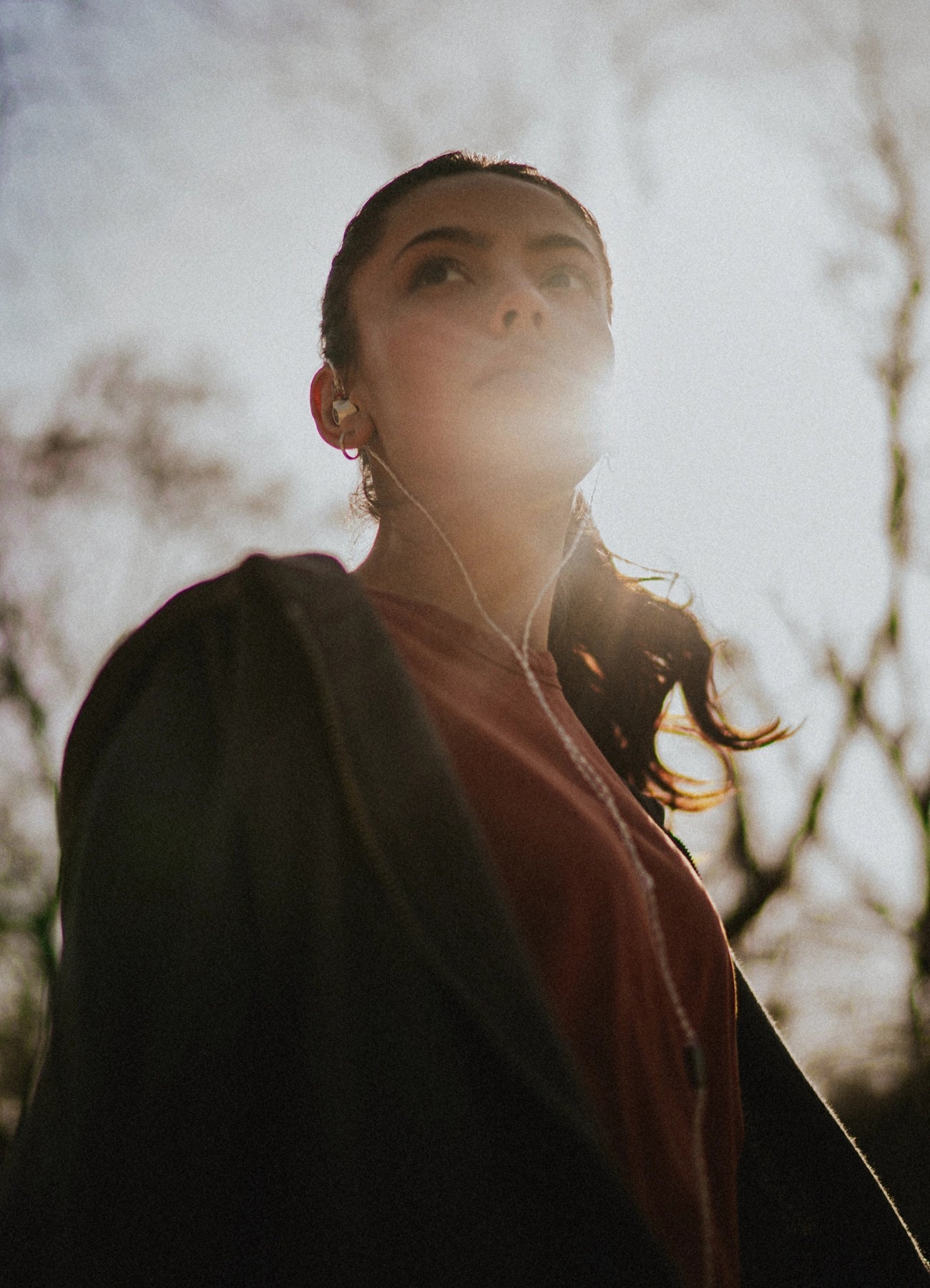 Young woman wearing the Meze Audio Alba best wired earbud headphones view from below with the Sun in the back