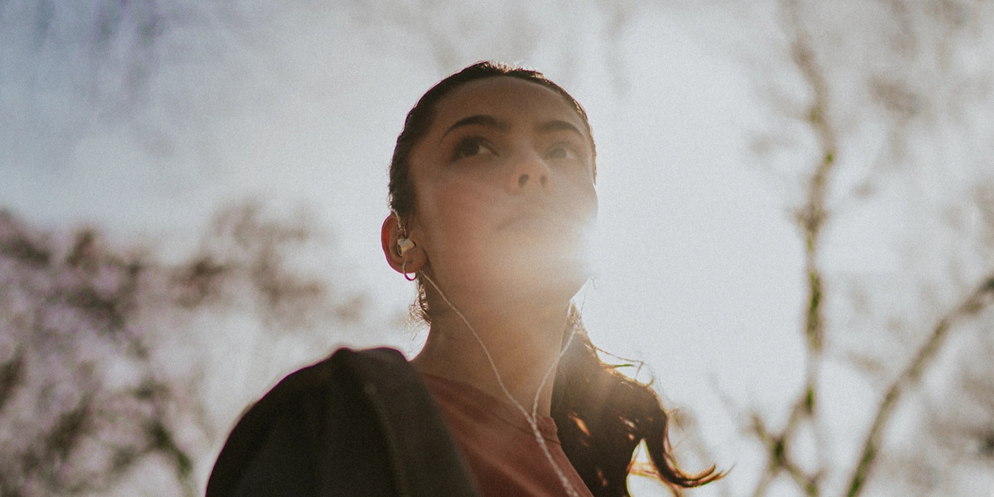 Young woman wearing the Meze Audio Alba best wired earbud headphones view from below with the Sun in the back