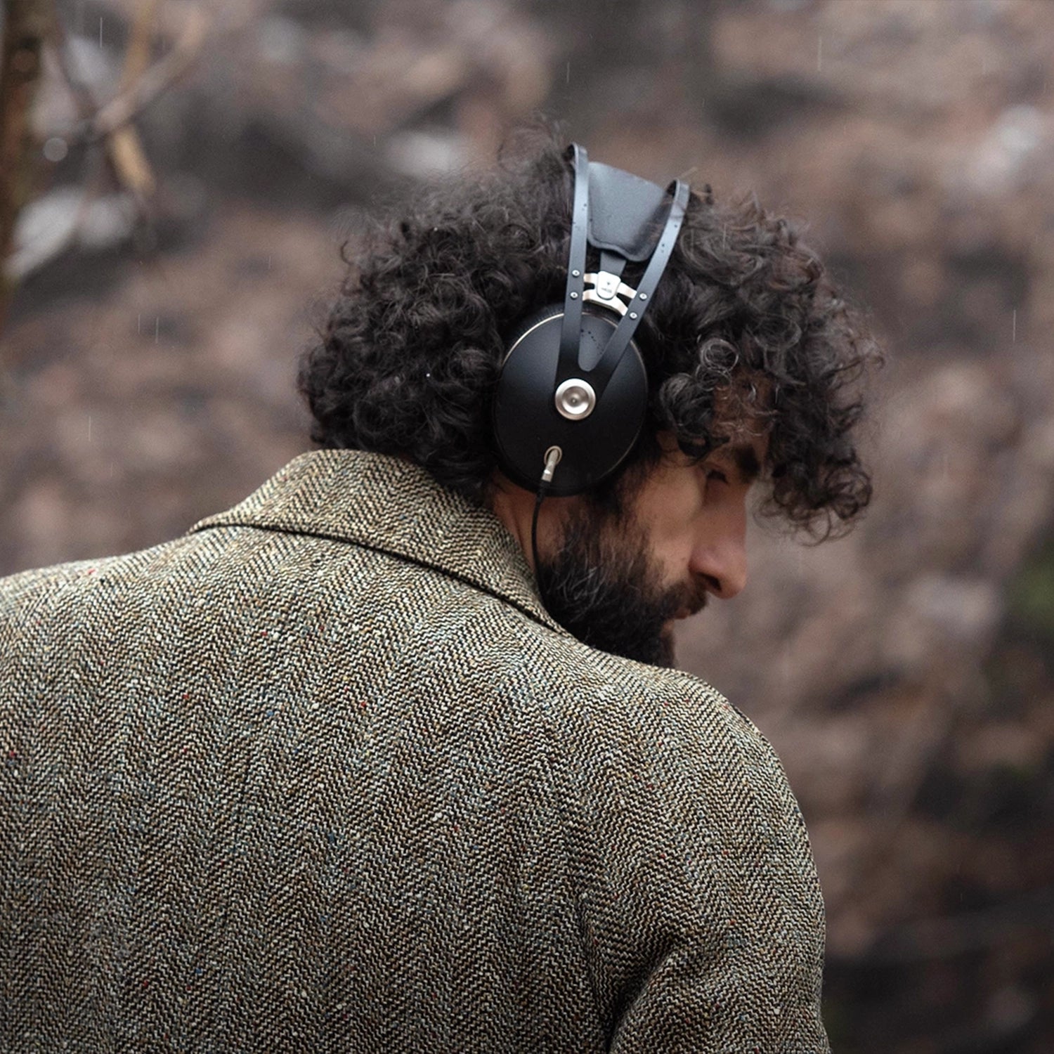 Man in grey coat sitting outside and listening to music on his Meze Audio 99 NEO wired head phones