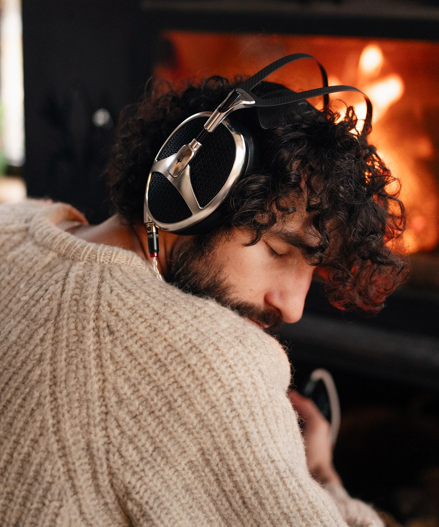 Man listening in front of the fireplace to Meze Audio Elite Aluminium planar magnetic open back audiophile headphones