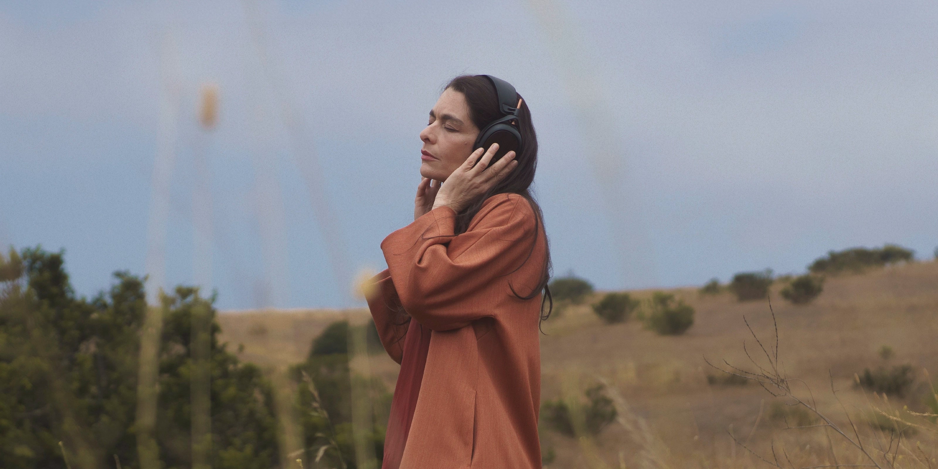 Woman in a field listening to her Meze Audio Liric closed-back audiophile hi-fi headphones