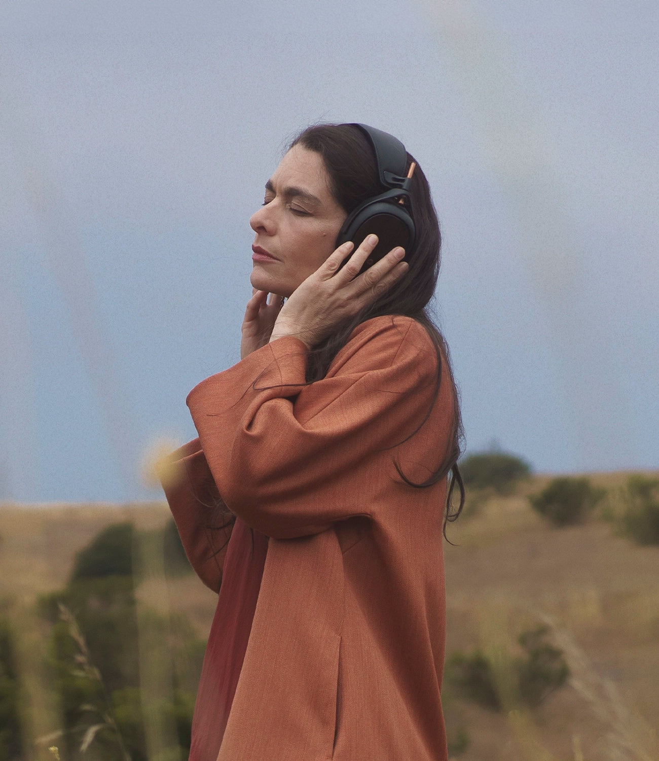 Woman in a field listening to her Meze Audio Liric closed-back audiophile hi-fi headphones